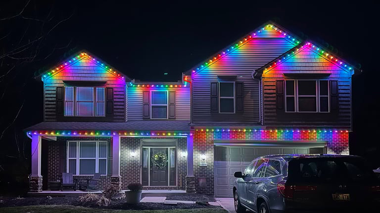 Two-story suburban home decorated with vibrant rainbow LED Christmas lights at night.
