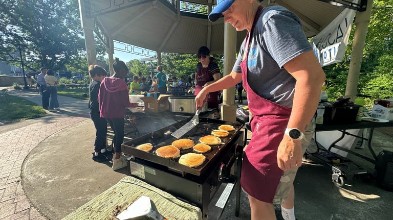 Kids in the background of a person flipping pancakes on a griddle in a park