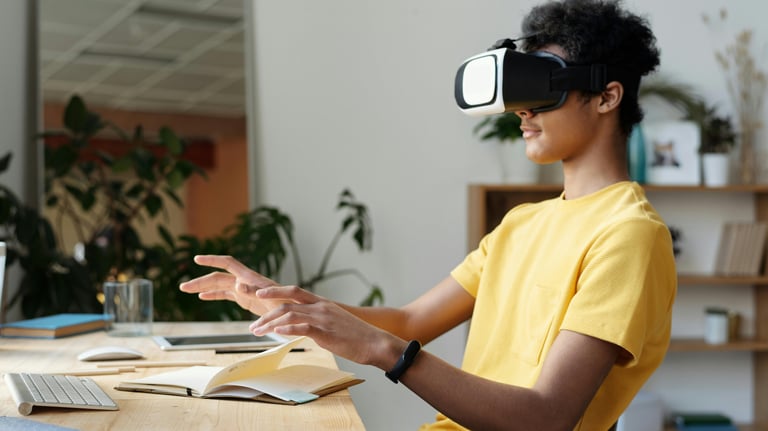 Lifestyle image of a student wearing VR headset, yellow t-shirt, and sitting at a cluttered desk.