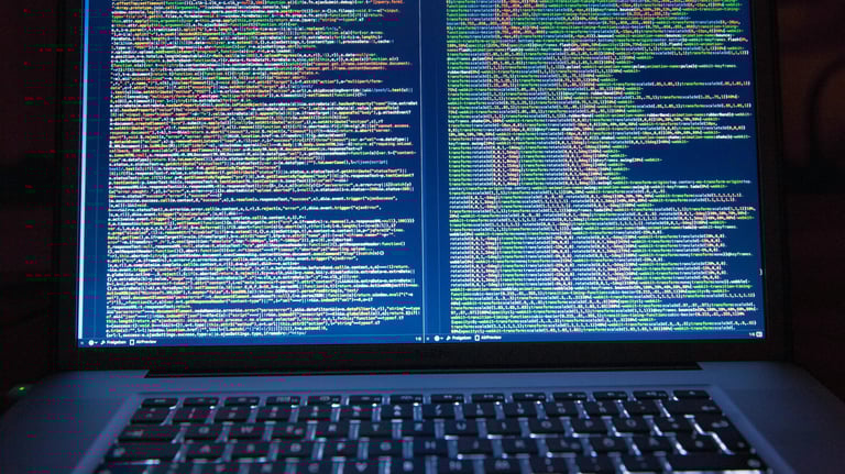 Lifestyle image of a laptop keyboard and screen with colorful yellow, green, and blue coding text.