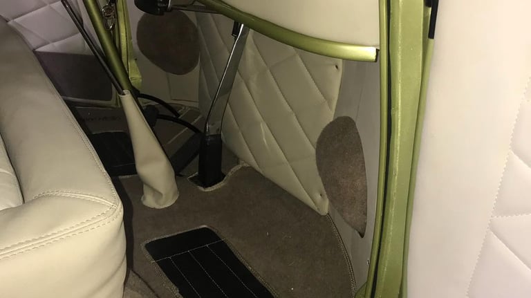 Vista da área da cabine dianteira da Kombi. Inclui um tapete customizado com o logotipo 'KOMBI'.