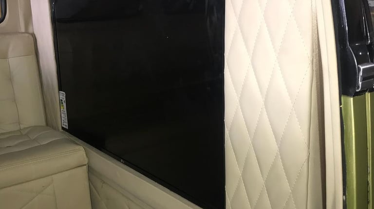 Uma TV de tela plana embutida em um painel creme claro customizado no interior da Kombi.