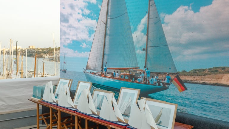 Pantalla led de fondo con imagen de barco navegando y delante mesa con trofeos y cuadros de fotos