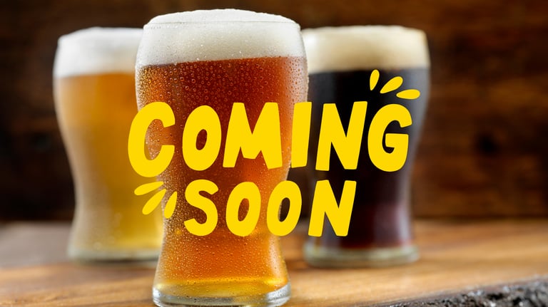 Three cold craft beers with condensation and foam under a yellow Coming Soon announcement text.