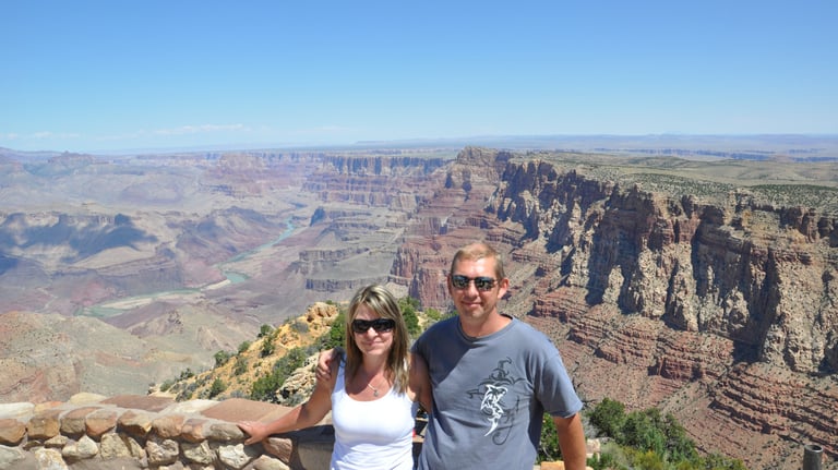 a man and woman standing on a cliff overlooking the grand canyon