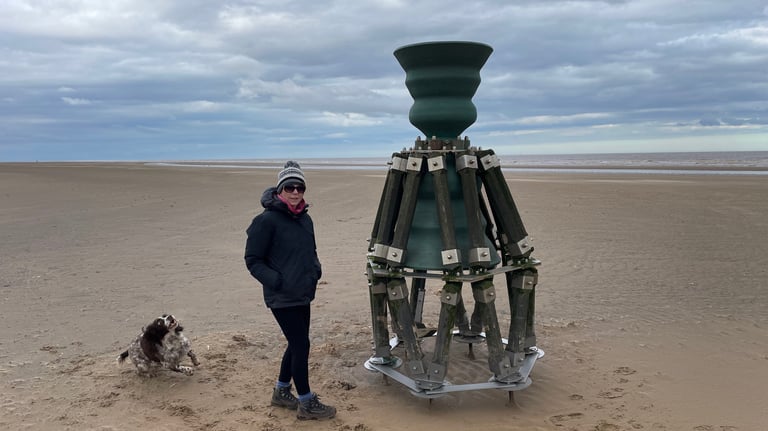 Tracey Billington standing by the time and tide bell on mablethorpe beach