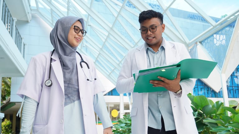 Dua tenaga medis berdiskusi sambil memeriksa dokumen di lingkungan rumah sakit modern