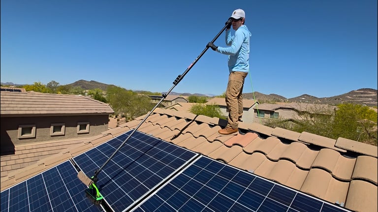 man standing on roof washing solar panel