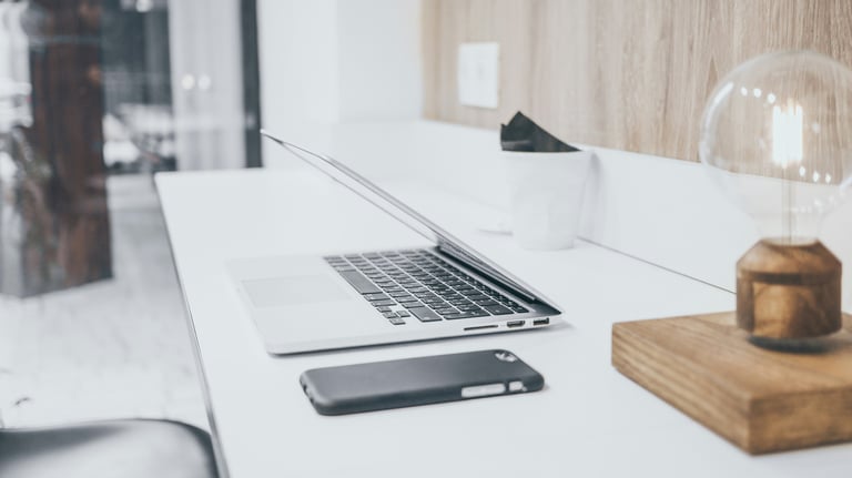 A laptop and smartphone placed on a wooden desk, showcasing a modern workspace setup.