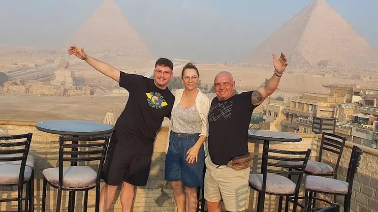 Foto de família de turistas do Brasil na varanda de um hotel em Gizé, observando o complexo das Pirâmides e a Grande Esfinge 
