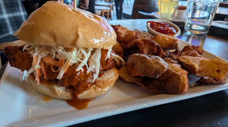 Crispy fried chicken sandwich with coleslaw served with potato wedges and ketchup on a white plate.