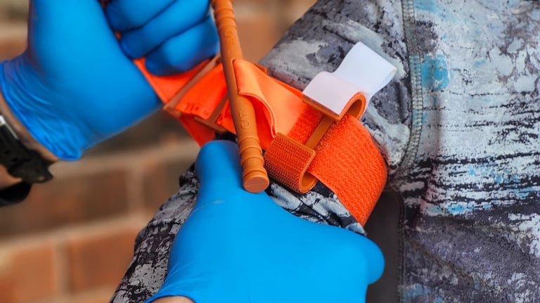C.A.T. 7, tourniquet being applied to arm during training using two hands wearing blue nitrile glove