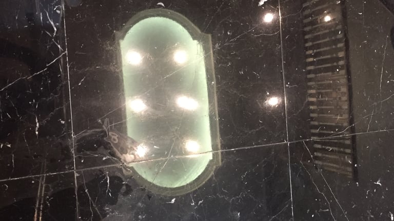 Overhead lighting and upper floor railing reflected right back in shinny black marble flooring