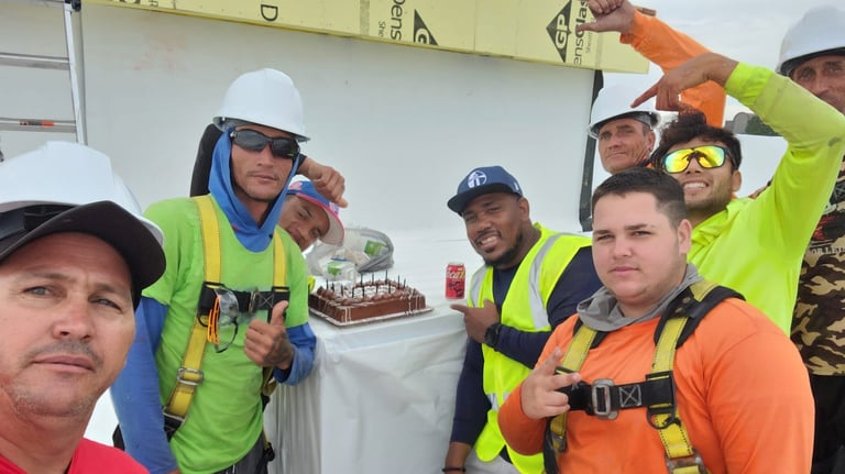 Construction workers in hard hats and safety vests celebrating with a chocolate cake on a job site.