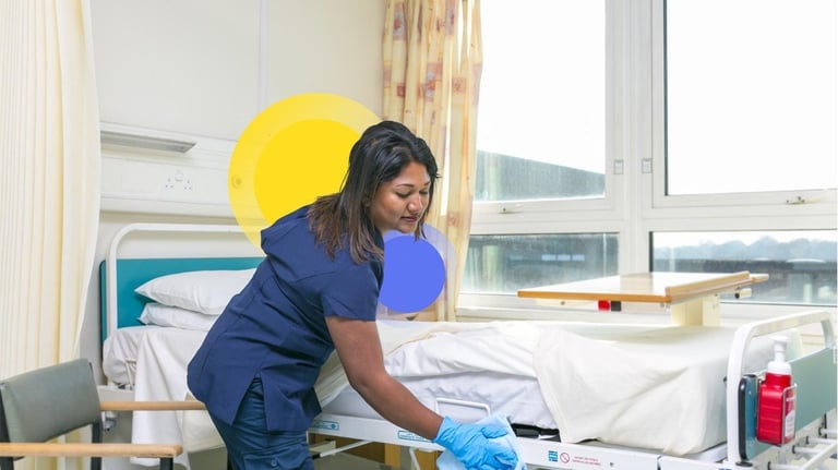 a nurse in scrubs and gloves cleaning a patient's bed