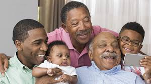 Four generations of an African American family smiling together while looking at a smartphone.