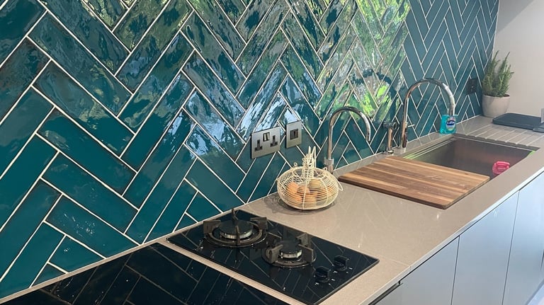 A kitchen backsplash with teal tiles laid in a herringbone style.