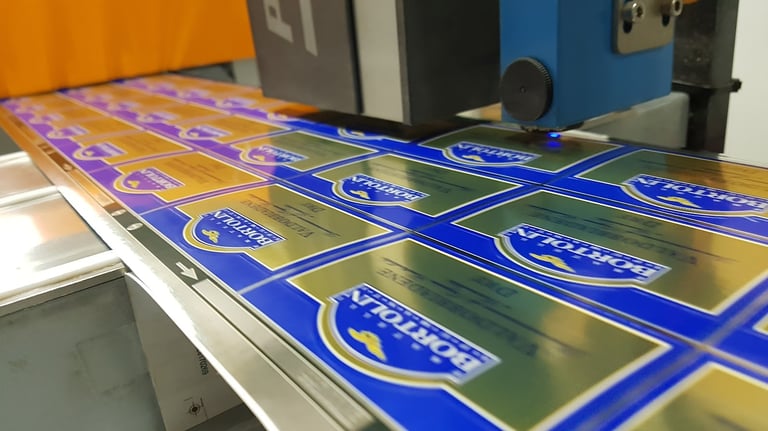 Industrial machine printing blue and gold Bortolin beverage labels on a high-speed production line.