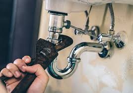 Plombier réparant un siphon d'évier métallique qui fuit à la clé à griffes.