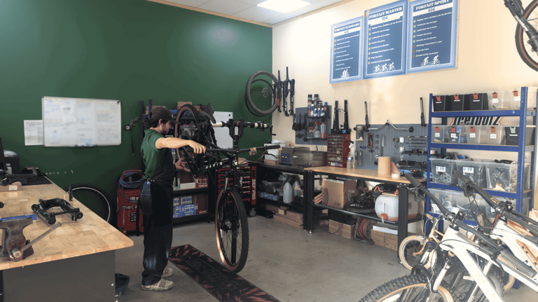 Professional bicycle mechanic repairing a mountain bike on a stand in a fully equipped bike workshop.