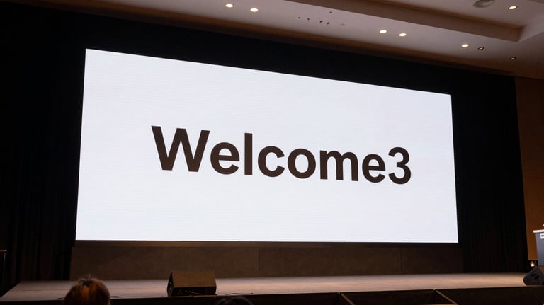 A wide shot of a corporate stage in a North American / US conference center. The screen displays 'Welcome' in a Montserrat font. The lighting uses warm bronze and dark charcoal tones.