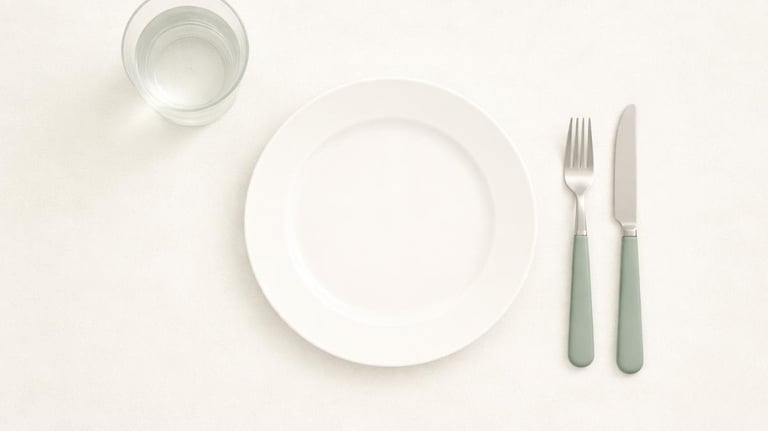 Farfurie goală văzută de sus, cu tacâmuri și un pahar cu apă, simbol al relației dificile cu alimentația