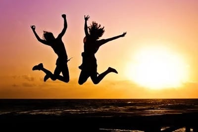 Two women's silhouettes jumping joyfully at sunset on the beach, full of energy