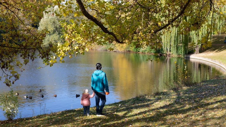Bild von einer erwachsenen Person, die mit einem Kind an der Hand an einem See spazierengeht.
