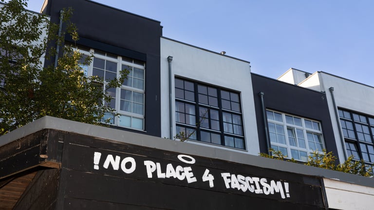 Bild von schwarzen und weißen Häusern, im Vordergrund ist das Graffitti "No room for facism".