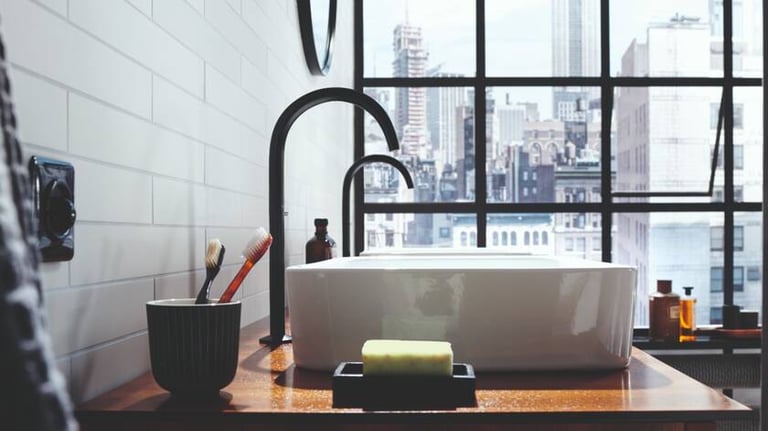 Modern bathroom vanity with a white vessel sink, matte black faucet, and a city view through a large window.