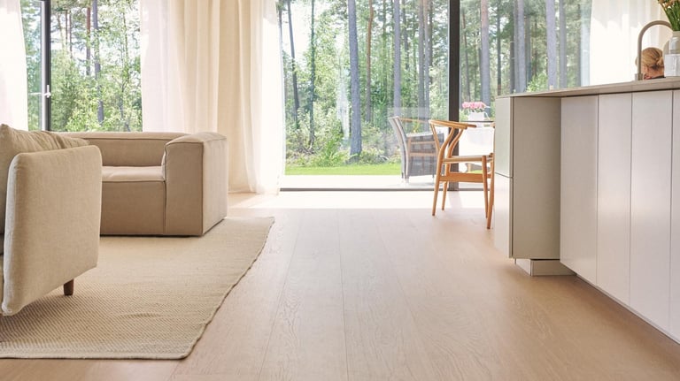 Modern open plan living room featuring light oak hardwood floors and large windows overlooking a forest.