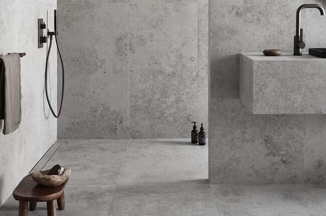 Modern minimalist bathroom featuring grey stone-effect tiles on walls and floors with black matte fixtures.