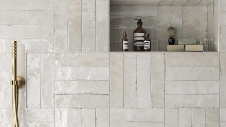 White gloss subway tile shower wall with gold hardware and built-in storage niche.