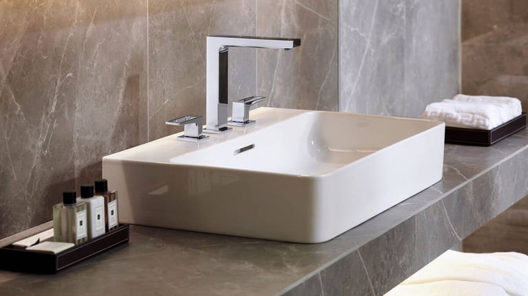 Modern white vessel sink with a chrome three-piece faucet on a grey marble bathroom vanity.