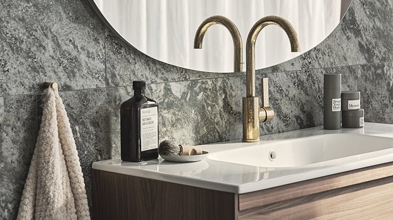 Modern bathroom vanity with a gold faucet, white sink, and grey marble tile backsplash.