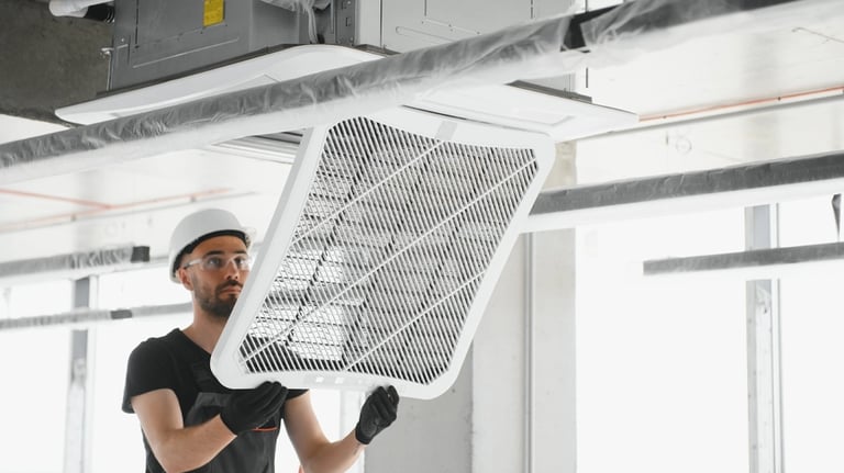 Technician in a hard hat installing a ceiling cassette air conditioning unit and filter.