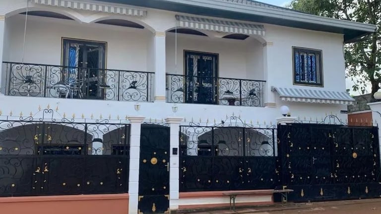 Maison blanche à étage, balcons en fer forgé noir et portail de sécurité assorti.