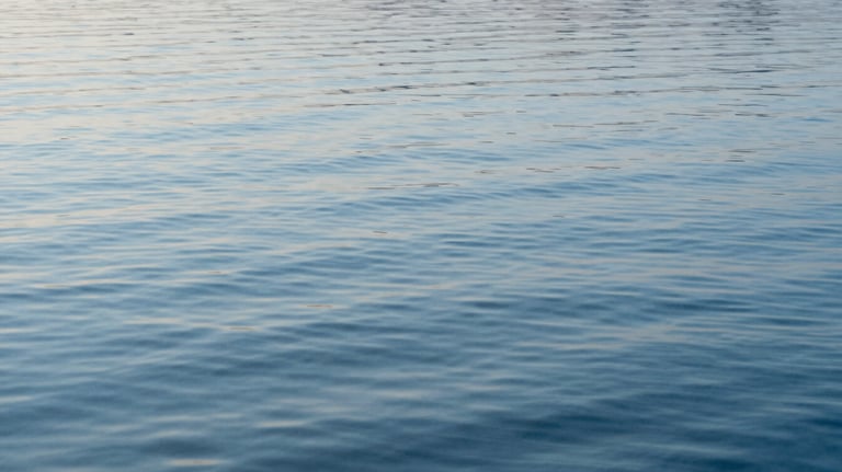 A serene photography of calm water ripples reflecting a light sky blue sky. The image is clean, abstract, and represents clarity and emotional well-being.