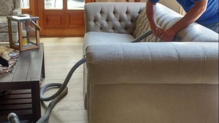 Professional upholstery cleaner deep cleaning a tufted beige sofa with a steam vacuum machine.