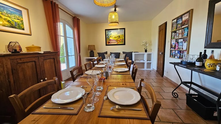 Table de la salle à manger mise pour le repas du soir, ton des murs crème et rideau ocre rouge.