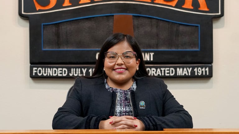 a woman in a black jacket and glasses sitting at a podium