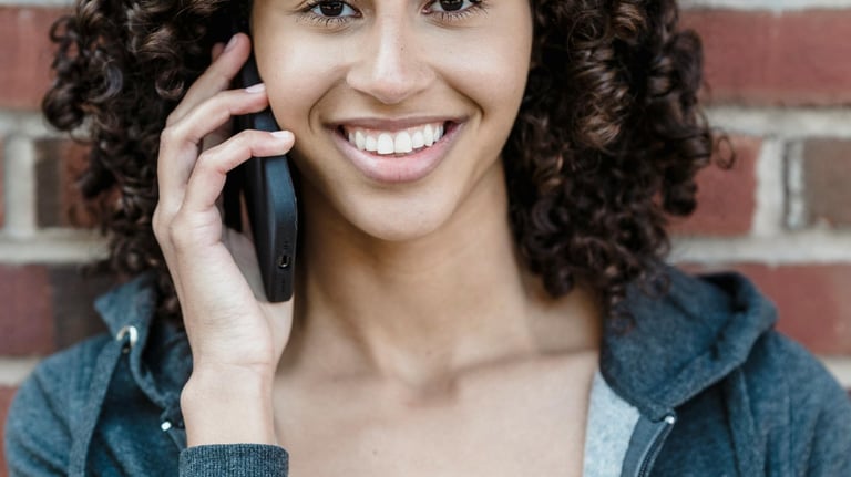 a woman with curly hair and a gray jacket. She's smiling and talking on the phone.