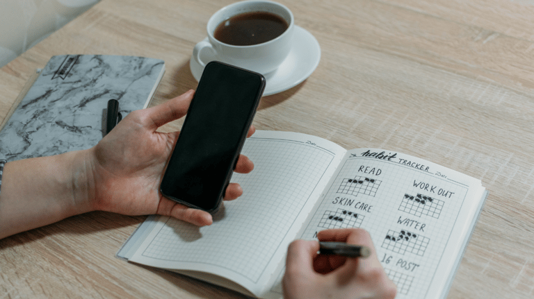 a person holding a cell phone and writing on a notebook