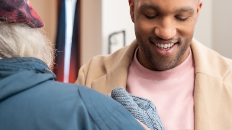 A male caregiver helps a male elderly client put on gloves