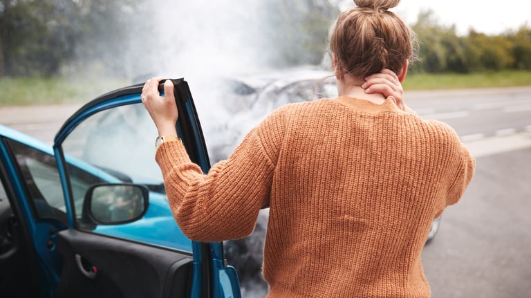 Woman holding neck after car accident with two cars facing each other and smoke coming from one car.