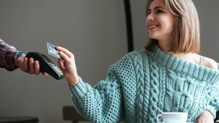 Smiling woman using a credit card for a contactless payment on a mobile card reader in a cafe.