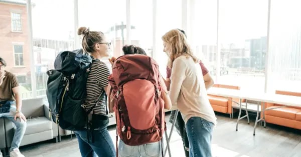 A group of young backpackers talking in a modern hostel lounge while planning their travel route.