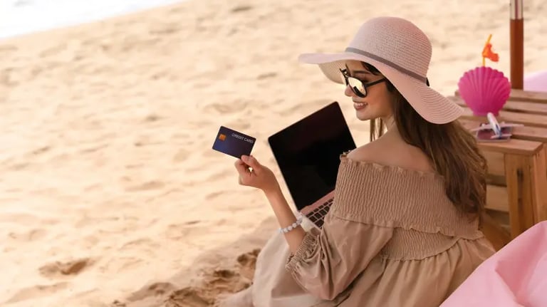 Woman using a credit card and laptop for online shopping while relaxing on a sandy beach.