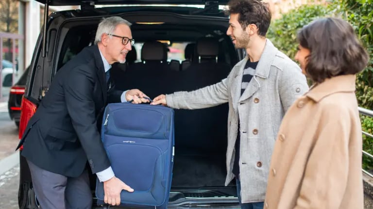 Professional chauffeur assisting a young couple by loading blue luggage into a black van.
