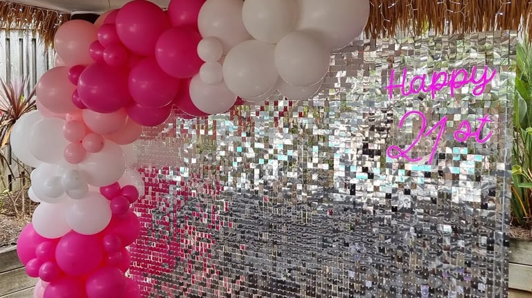 Silver shimmer wall with pink and white balloon garland and happy 21st neon sign.